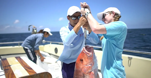 Two people holding up a fish on a boat.