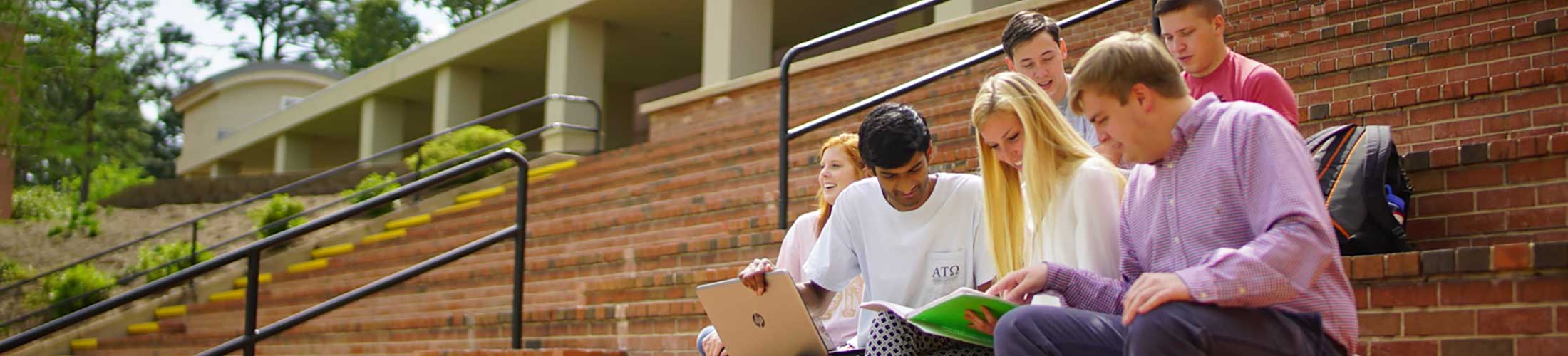 Group of students studying sitting on stairs on campus.