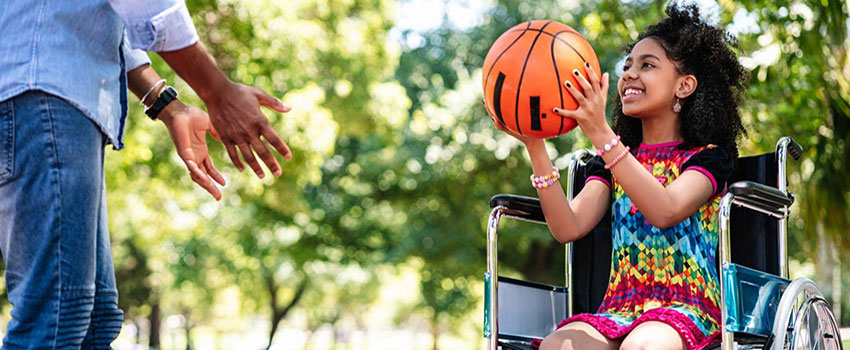 Young girl in wheelchair playing basketball with an adult.