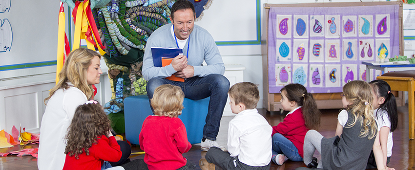 Man holding book talking to children sitting on the floor.