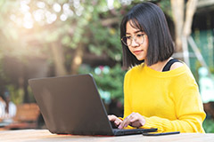 Woman sitting and working on laptop outside.