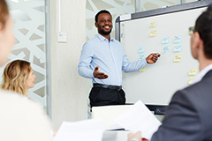 Man smiling pointing to white board while people look on.