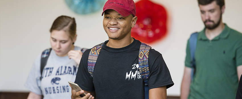 A male student smiling and walking out of a Nursing class