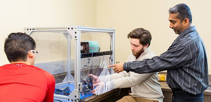 Electric Engineering students working on a machine with professor.