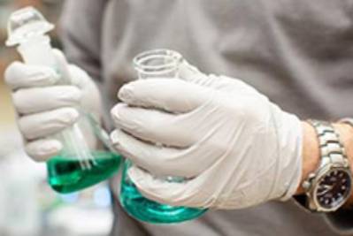 Gloved hands holding beakers in lab.