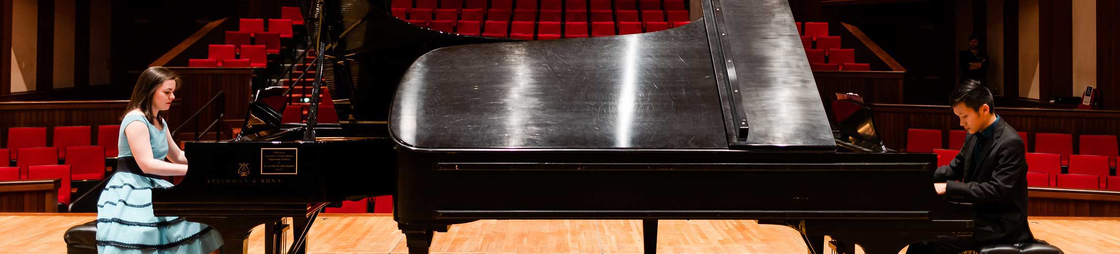 Two students playing piano on stage.