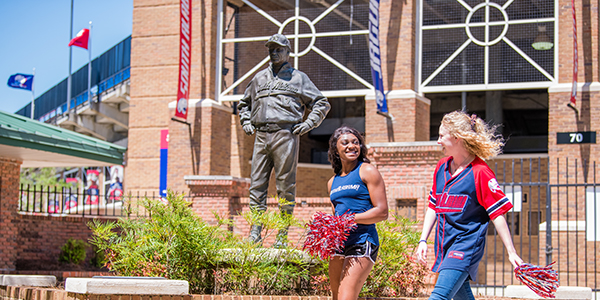 Two students walking outside of the stadium holding pom poms.