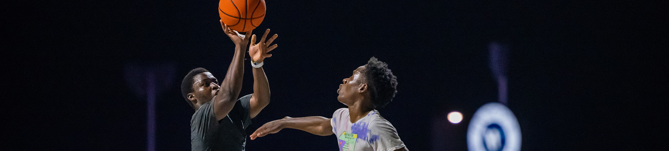 Two students playing basketball with Hancok Whitney in background.