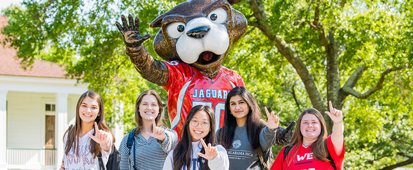 Students holding up J sign in front of Southpaw statue.