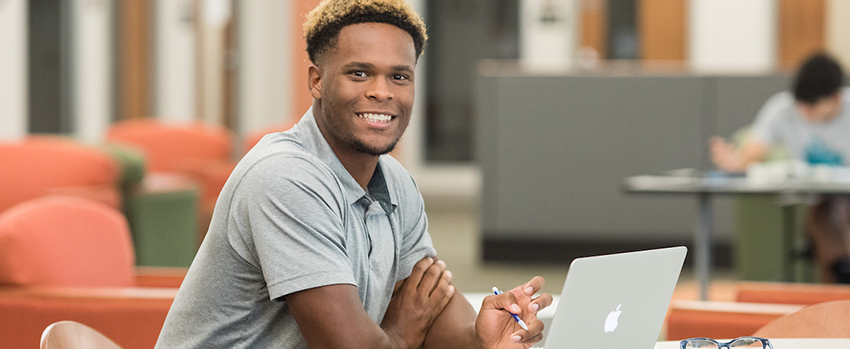 Male student sitting at desk working on a laptop.