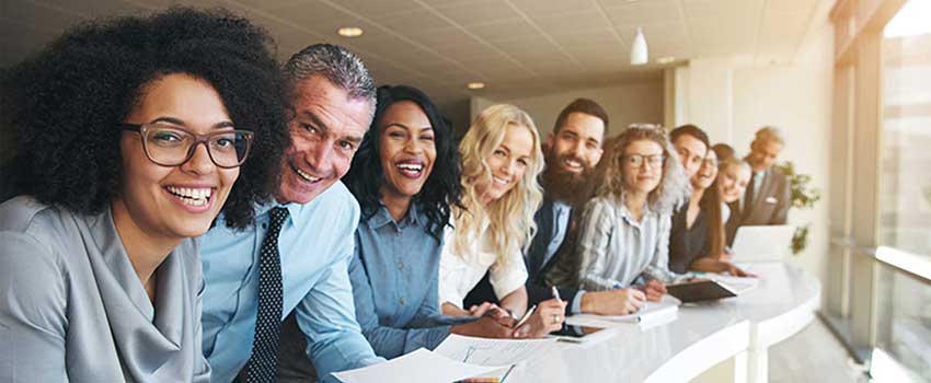 A group of people smiling leaning on counter taking notes.