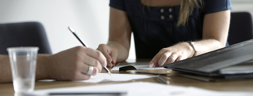 People writing on paper on table.