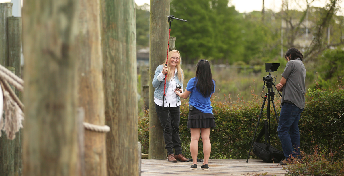 Dr. Lorraine Ahearn, an assistant professor of multimedia journalism at the University of South Alabama, holds a boom microphone for her interview with Hang Nguyen, who moved to Bayou La Batre from Vietnam as a child. Ahearn is producing a documentary about the Vietnamese fishing community on the Alabama Gulf Coast. The videographer on many of her interviews is Francisco Cordova, right, a December graduate from the digital cinema and television program. data-lightbox='featured'